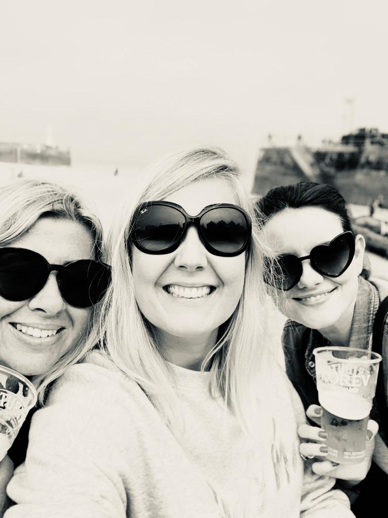 Close up in black and white of Reside Living founders, Mel, Mic and Michelle together at the beach with drinks in hand